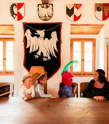 Children in knight costumes playing in a medieval-themed room with coats of arms and wall tapestries. | © Zell am See-Kaprun Tourismus