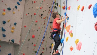 A child climbing in an indoor climbing wall with colorful holds. | © Zell am See-Kaprun Tourismus