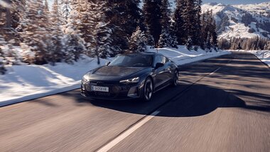 A black car driving on a snow-covered road through a winter mountain landscape. | © Audi, Tom Klocker
