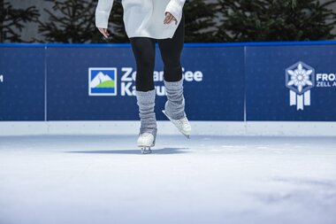 Close-up of a person ice skating on an ice rink, showing skates and leg clothing. | © Zell am See-Kaprun Tourismus