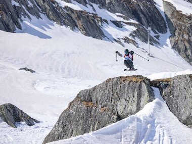 Skier on a snowy mountain ridge with steep rocks and glaciers in the background. | © Andy Putz