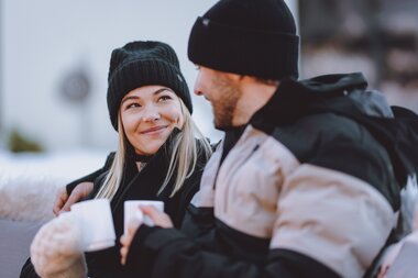 Two people in winter clothing and hats talking outdoors, with a snowy landscape in the background. | © EXPA JFK