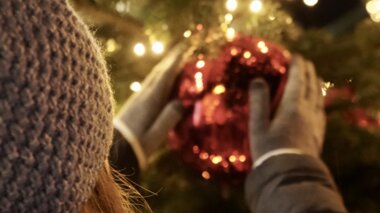 Person decorating a Christmas tree with a large red bauble surrounded by string lights. | © Zell am See-Kaprun Tourismus