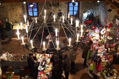 View of a cozy Christmas market in a rustic stone hall with a variety of Advent items and decorations. | © MediaProductionBK