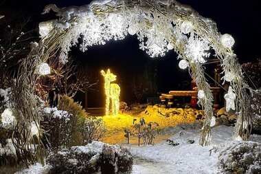 Christmas-themed entrance in snow with illuminated reindeer figure and decorated archway of string lights | © Grand Hotel Zell am See