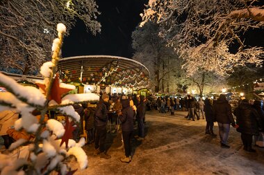 Christmas market at Zeller See during a winter evening with people and decorative lights. | © Zell am See-Kaprun Tourismus