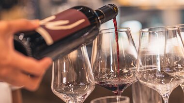 A person pouring wine into a glass during a tasting. Other glasses are visible in the background. | © Johannes Radlwimmer