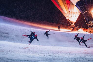 People skiing at night with illuminated hot air balloons in the background during nighttime. | © EXPA JFK