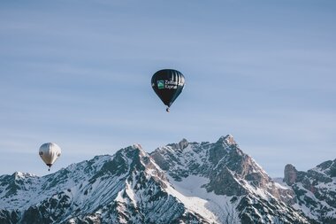 Multiple hot air balloons floating in front of snow-covered mountain peaks during Balloonalps 2024 near Zell am See-Kaprun. | © Zell am See-Kaprun Tourismus