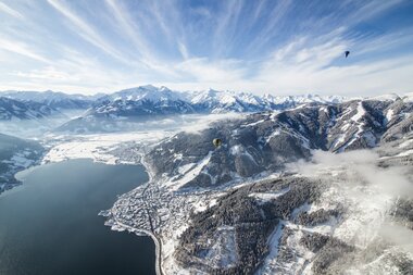 Aerial view with hot air balloons over snow-covered mountains and a lake in a winter landscape. | © artisual