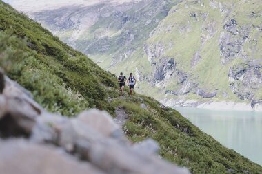 Participants running along a high mountain reservoir during the Ultra Trail near Kaprun, Austria. | © EXPA OBH