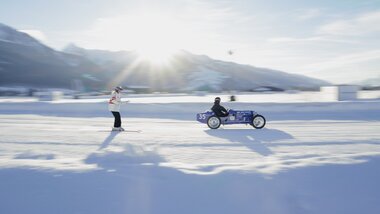 An ice race with a skier being pulled by a racecart on a snow-covered track under sunlight. | © GP ICE RACE, David Papenheim