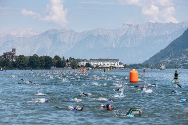 Swimmers competing in a race in the water with mountains and forests in the background. | © Zell am See-Kaprun Tourismus