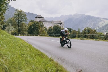 A cyclist during IRONMAN 70.3 in Zell am See-Kaprun on a winding road amidst scenic mountain landscape. | © Zell am See-Kaprun Tourismus