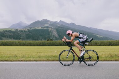 A cyclist participating in an Ironman 70.3 event in Zell am See-Kaprun, surrounded by mountains and green landscape. | © Zell am See-Kaprun Tourismus
