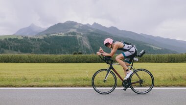 A cyclist participating in an Ironman 70.3 event in Zell am See-Kaprun, surrounded by mountains and green landscape. | © Zell am See-Kaprun Tourismus
