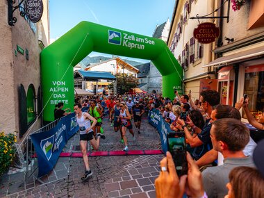 Start of a night run event in Zell am See-Kaprun with many participants under a large green start arch. | © Zell am See-Kaprun Tourismus