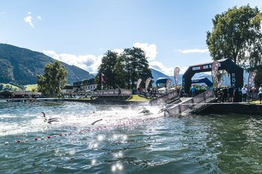 Start of the IRONMAN 70.3 Zell am See-Kaprun 2025 with athletes diving into the lake on a sunny day. | © Zell am See-Kaprun, JOE