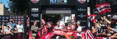 Winner crossing the finish line at IRONMAN 70.3 Zell am See-Kaprun 2025, surrounded by cheering fans and organizers. | © Zell am See-Kaprun, JOE