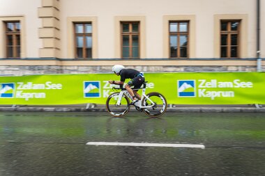 Cyclist in a race riding on a wet road in front of historic buildings in Zell am See. | © Zell am See-Kaprun Tourismus
