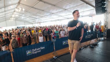 Host on stage at a line dance event inside a tent, with audience in the background. | © Zell am See-Kaprun, JOE