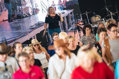 People line dancing at AlpFestival 2025, day 2, on a stage with music equipment in the background. | © Zell am See-Kaprun, JOE