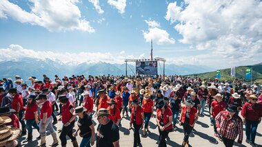 Large crowd at the Alpine Festival participating in line dance, mountains in the background and a sunny sky. | © Zell am See-Kaprun, JOE