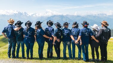 Group of people doing line dance on a green meadow with mountains in the background. | © Zell am See-Kaprun, JOE