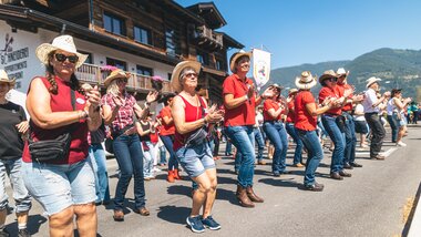 Participants line dancing at the AlpFestival 2025 outdoors in front of traditional buildings on a sunny day. | © Zell am See-Kaprun, JOE