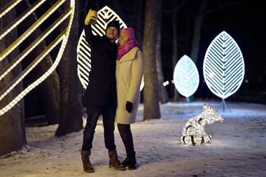 Two people posing in a winter park at Lumagica, surrounded by illuminated sculptures and decorations. | © MediaProductionBK