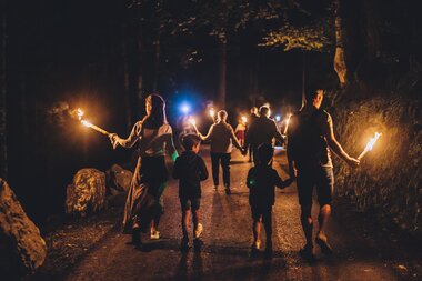 Family and friends on a nighttime torch walk in the forest, illuminated by fire and lights. | © EXPA, Jürgen Feichter