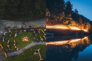 Campfire and people at a night event by the water, with a lit bridge in the background, reflected in the water. | © EXPA FEI