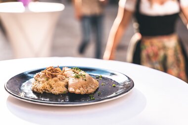 Traditional dish on a black plate featuring potatoes, meat, and herbs at a summer night event. | © Zell am See-Kaprun Tourismus