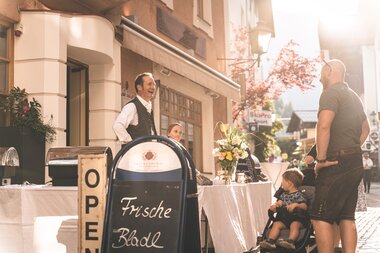 Event at the summer night festival with a transparent table, a smiling craftsman, a small person sitting on the ground, and a man talking on the street side. | © Zell am See-Kaprun Tourismus