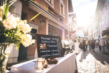 Street market at summer night festival with a stall, sunshine, and many people in a historic town. | © Zell am See-Kaprun Tourismus