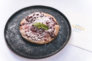 A traditional Austrian dessert dusted with powdered sugar, decorated with a mint leaf, served on a black plate. | © Zell am See-Kaprun Tourismus