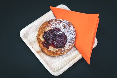 Small sweet dish with berry jam on a wooden board, accompanied by an orange napkin. | © Zell am See-Kaprun Tourismus