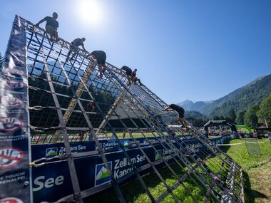 Participants of the Spartan Race climbing a steep, slippery ramp with safety nets in a mountain landscape. | © Christoph Oberschneider