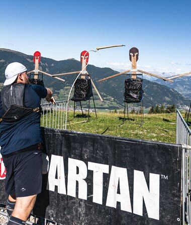 Participant training at a Spartan Race with target figures in the background, set on a hillside with mountains in the distance. | © Zell am See-Kaprun Tourismus