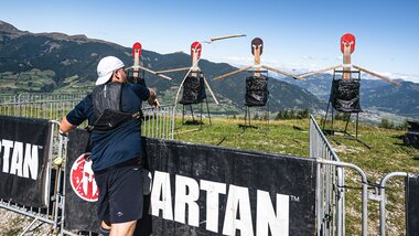 Participant training at a Spartan Race with target figures in the background, set on a hillside with mountains in the distance. | © Zell am See-Kaprun Tourismus