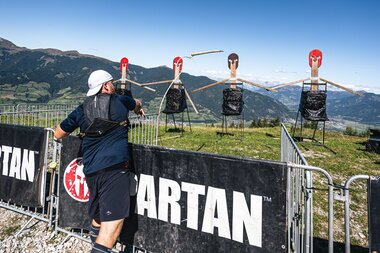 Participant training at a Spartan Race with target figures in the background, set on a hillside with mountains in the distance. | © Zell am See-Kaprun Tourismus