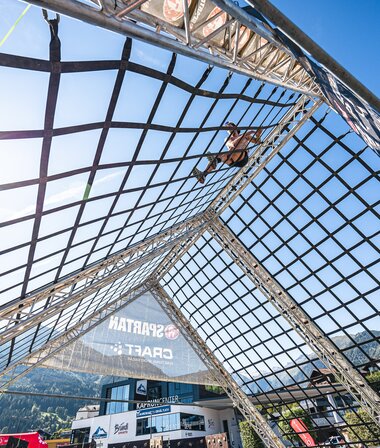 A participant at a Spartan Race climbing or running over a large net structure under a bright sky. | © Zell am See-Kaprun Tourismus