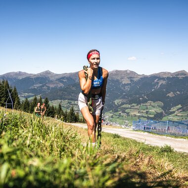 Participant in the Spartan Race in Zell am See-Kaprun, surrounded by mountains and green landscape, running on a mountain meadow during the race. | © Zell am See-Kaprun Tourismus