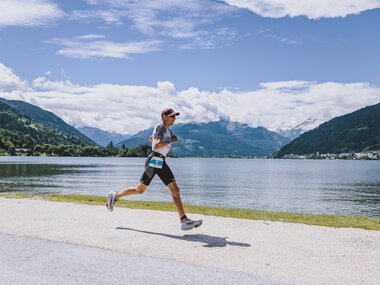 Runner jogging along the shore of a lake in Zell am See, surrounded by mountains under a clear sky. | © EXPA, Jürgen Feichter
