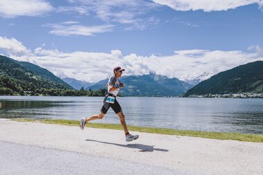 Runner jogging along the shore of a lake in Zell am See, surrounded by mountains under a clear sky. | © EXPA, Jürgen Feichter