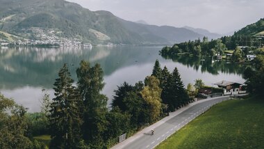 Scenic view of a lake surrounded by mountains, with a road in the foreground and a calm sky. | © Zell am See-Kaprun Tourismus