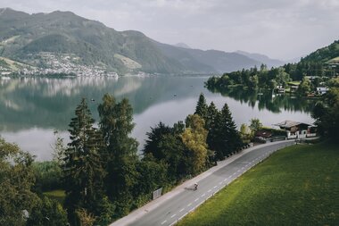 Scenic view of a lake surrounded by mountains, with a road in the foreground and a calm sky. | © Zell am See-Kaprun Tourismus