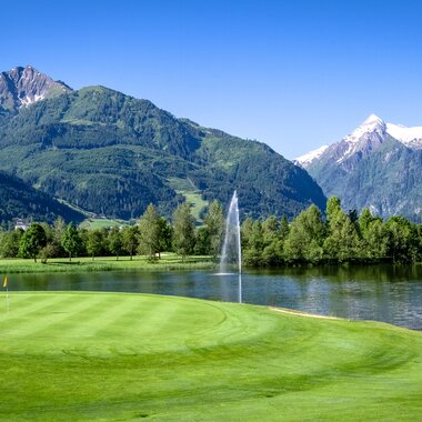 A golf course with green fairways, mountains in the background, and a waterfall in a scenic landscape. | © Golfclub Zell am See