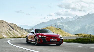 Red sports car driving on a winding road through mountainous landscape with mountains and clouds in the background. | © Agentur LOOP New Media GmbH