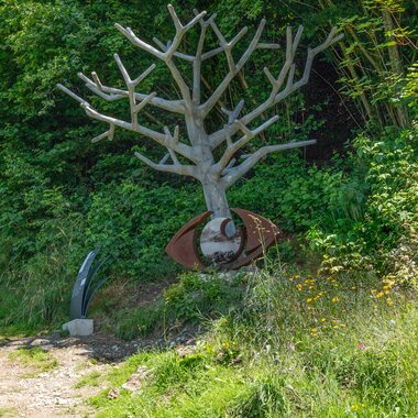 Metal tree sculpture in a green garden with bushes and flowers. | © Edith Danzer